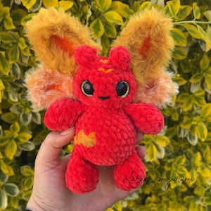 Pu&ograve; includere: Un piccolo peluche lavorato all'uncinetto a mano con un corpo in filato rosso brillante e testurizzato e grandi ali soffici in pelliccia sintetica color arancio dorato. La creatura ha due grandi occhi di sicurezza neri lucidi con glitter oro.