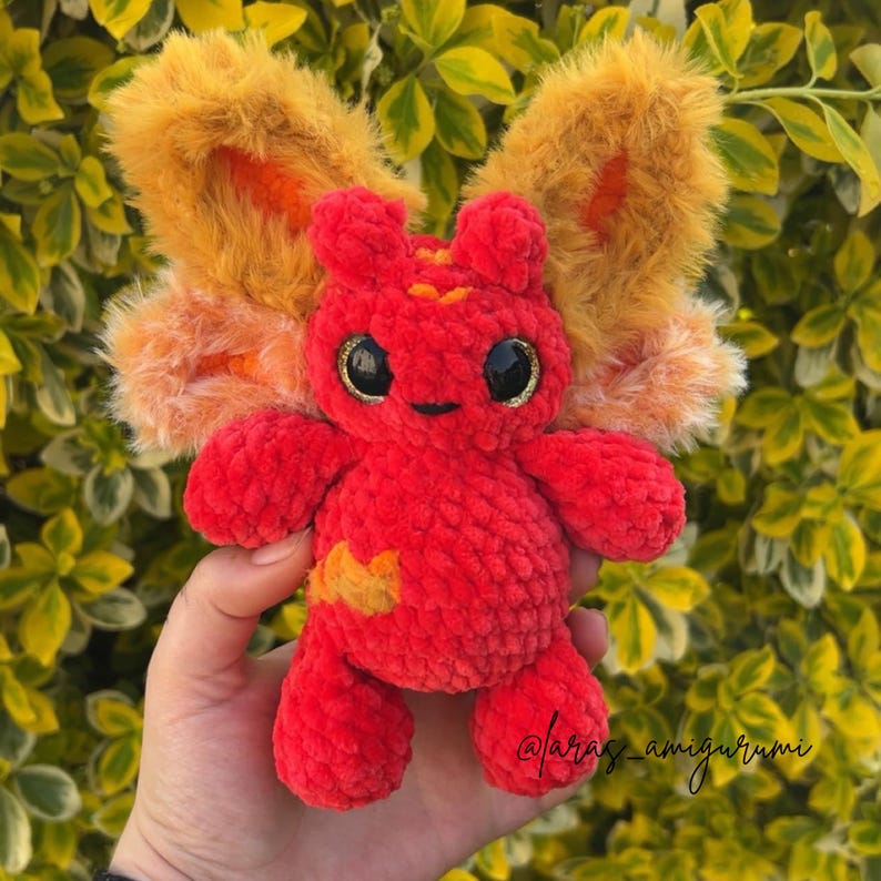 Pu&ograve; includere: Un piccolo peluche lavorato all'uncinetto a mano con un corpo in filato rosso brillante e testurizzato e grandi ali soffici in pelliccia sintetica color arancio dorato. La creatura ha due grandi occhi di sicurezza neri lucidi con glitter oro.