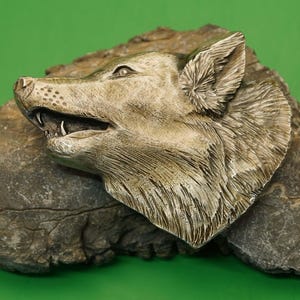 Op de afbeelding: Een gedetailleerd zilveren beeld van een wolfskop, met een textuur van bont, gemonteerd op een ruwe, grijze rots.