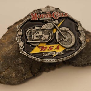 May include: A silver belt buckle featuring a black and white image of a vintage motorcycle with the text "The Motor Cycle Founded 1903" and "BSA Golden Flash 650 Twin"
