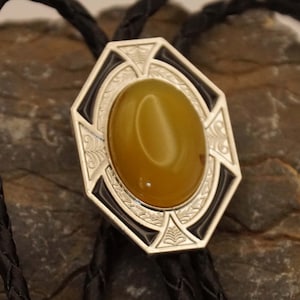 Könnte beinhalten: Ein silberner Bolo-Schlips mit einem schwarzen und weißen gravierten Design und einem gelben Achat-Stein in der Mitte.