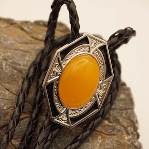May include: A black leather bolo tie with a silver and black octagonal pendant featuring a large, bright yellow oval gemstone.
