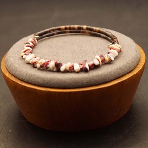 May include: A brown leather bracelet with a row of red, white and brown shell beads.