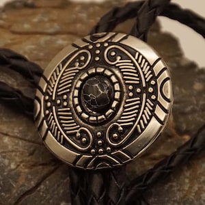 Bolotie rund mit schwarzem Stein im Schild mit ornamentalen Motiven