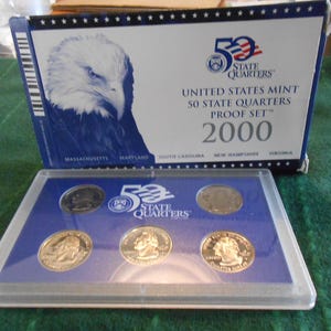 May include: A 2000 United States Mint 50 State Quarters Proof Set. The box features an eagle illustration and the text "50 State Quarters Proof Set 2000". The set includes six quarters in a clear plastic case, displayed on a blue background.