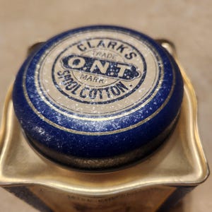 Puede incluir: Una lata azul y dorada con una etiqueta blanca que dice "Clarks Trade Mark ONT Spool Cotton."