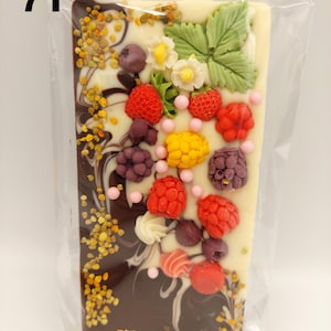 Op de afbeelding: Een rechthoekige chocoladereep met een tweekleurig ontwerp, donkerbruin aan de linkerkant en wit aan de rechterkant. De reep is versierd met diverse kleurrijke snoepjes, waaronder rode frambozen, aardbeien en gele maïsvormige snoepjes. Het nummer "71" staat linksboven.