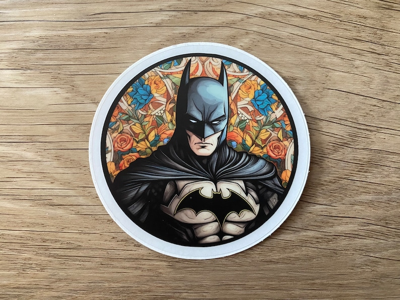Pu&ograve; includere: Un adesivo rotondo con un'illustrazione dettagliata di Batman in un costume blu scuro e nero, con un simbolo di pipistrello giallo sul petto. Lo sfondo &egrave; un motivo floreale colorato con fiori gialli, arancioni, rossi e blu.