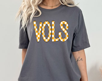 Könnte beinhalten: Ein graues T-Shirt mit einem karierten orange-weißen Aufdruck, auf dem vorne "VOLS" steht.