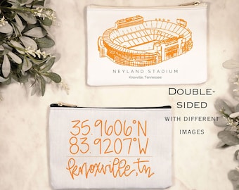 May include: Two white canvas zipper pouches. One features an orange illustration of Neyland Stadium, Knoxville, Tennessee. The other displays coordinates 35.9606°N 83.9207°W and the text "Knoxville, tn" in orange. The text "WHITE OR BLACK ZIPPER" is above the stadium pouch.