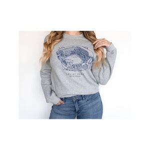 K&ouml;nnte beinhalten: Ein graues Sweatshirt mit einer blauen Umrandung des Truist Park, einem Baseballstadion in Atlanta, Georgia. Der Text "Truist Park" und "Atlanta, Georgia" ist unterhalb der Stadionumrandung aufgedruckt.