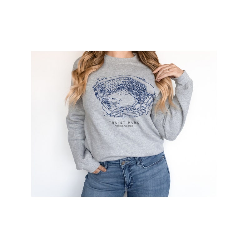 K&ouml;nnte beinhalten: Ein graues Sweatshirt mit einer blauen Umrandung des Truist Park, einem Baseballstadion in Atlanta, Georgia. Der Text "Truist Park" und "Atlanta, Georgia" ist unterhalb der Stadionumrandung aufgedruckt.