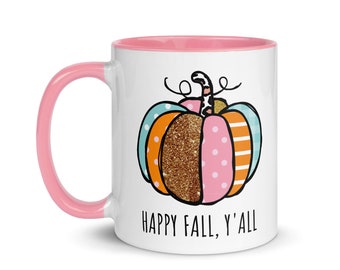 May include: White ceramic mug with a pink interior and handle. The mug features a colorful pumpkin design with polka dots, stripes, and glitter, and the text "HAPPY FALL, Y'ALL" in black.