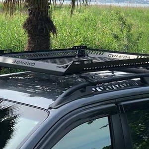 May include: A black metal roof rack with a mesh grid top is mounted on a black pickup truck. The roof rack has the text "AGMH4WD" and "GWANDA" printed on it.