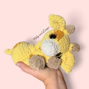 May include: A crocheted giraffe plush toy with yellow, brown, and white yarn. The giraffe has large, googly eyes and is lying on its side.