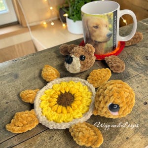 Könnte beinhalten: Ein handgefertigter Häkeltier-Untersetzer mit Sonnenblumenmuster, einem braunen Bärenkopf und einer Tasse mit einem Golden Retriever. Die Schildkröte hat gelbe und beige Akzente. Auf der Tasse steht "Golden Retriever".