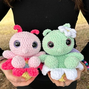 以下が含まれることがあります： 2つの編みぐるみタコ、1つは虹色のアクセントが付いたピンク、もう1つは白い花が付いたグリーン
