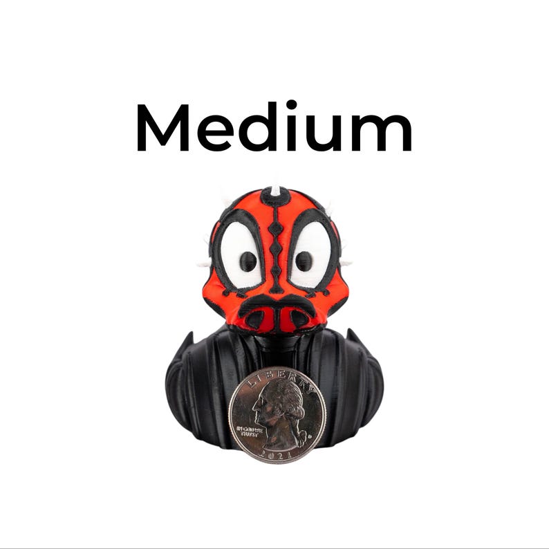 May include: A rubber ducky with a red and black face design, resembling a character from a science fiction film. The ducky has a black body and a quarter coin is in front of it. The word "Medium" is above the ducky.