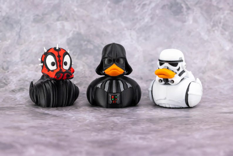 May include: Three rubber duck toys styled as Star Wars characters: Darth Maul, Darth Vader, and a Stormtrooper. The Darth Maul duck is red and black with white horns. Darth Vader is black with a black helmet. The Stormtrooper duck is white with a black helmet.
