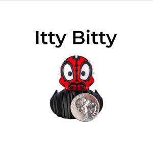 May include: A small, black and red figurine of a character with a quarter coin next to it. The figurine has a red face with black markings and white eyes. The text "Itty Bitty" is above the figurine.
