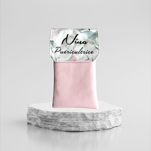 May include: A pink phone case with a white floral design and the text "Nina Puericultrice" printed on the front.
