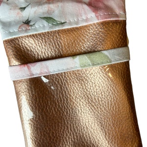 May include: A small, rose gold-colored pouch with a floral print lining. The pouch is made of faux leather and has a zipper closure.
