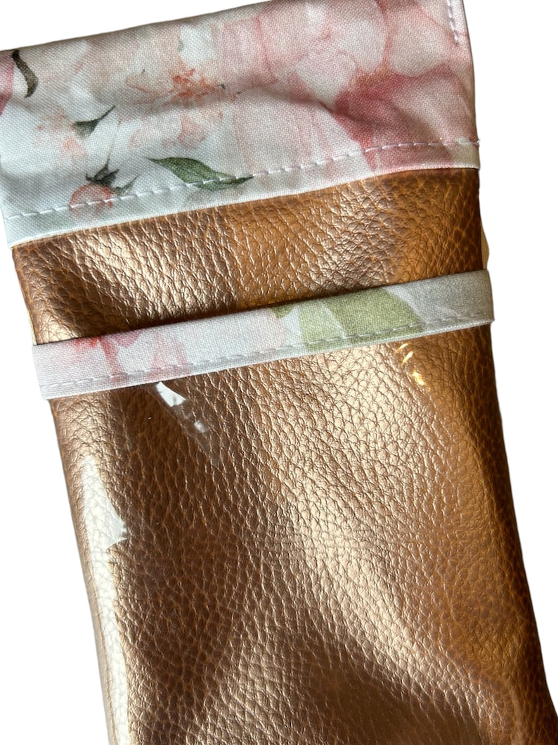May include: A small, rose gold-colored pouch with a floral print lining. The pouch is made of faux leather and has a zipper closure.