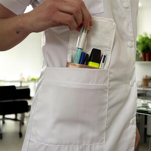 May include: A white lab coat with a large pocket on the front. The pocket is filled with pens and a highlighter.