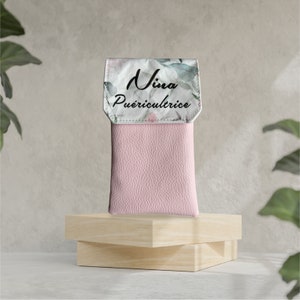 May include: A pink leather phone case with a white floral print and the text "Nina Pu&eacute;ricultrice" on the front.