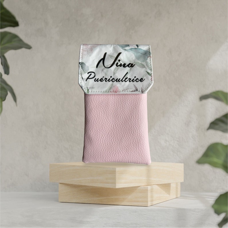 May include: A pink leather phone case with a white floral print and the text "Nina Pu&eacute;ricultrice" on the front.