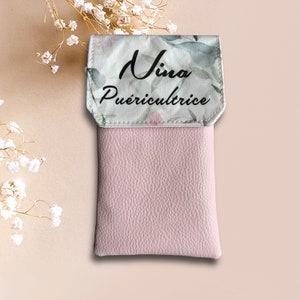 May include: A pink leather phone case with a white floral flap. The flap has the text "Nina Pu&eacute;riculture" printed on it.