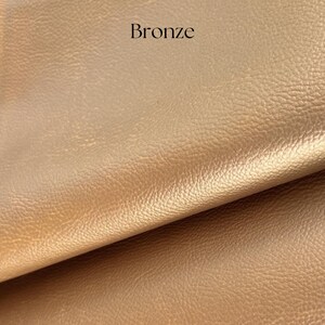 May include: A close-up of a piece of faux leather in a bronze color. The leather has a textured surface.