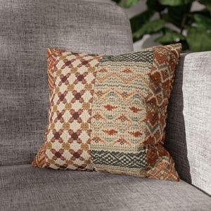 May include: A square throw cushion featuring a patchwork design with a mix of textured fabrics. The left side displays a brown and cream cross-stitch pattern, while the right side showcases a multi-coloured geometric print in orange, green, and tan.