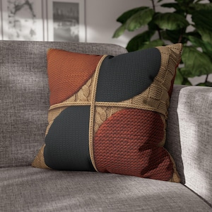 Puede incluir: Un cojín cuadrado con un diseño de cuatro cuadrantes que presenta secciones alternas de texturas de punto en color naranja quemado y gris carbón oscuro. Las secciones están separadas por un patrón de cruz en punto trenzado beige.