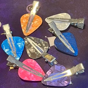 May include: Set of six guitar pick hair clips in various colours and patterns, including orange, blue, grey, white, pink, and purple.