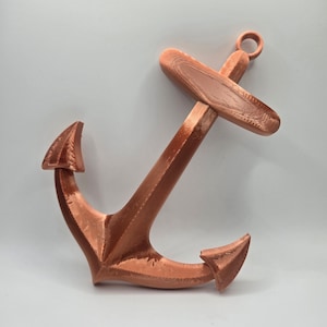 May include: A copper-colored metal anchor with a flat, rectangular top and two pointed arms. The anchor is a decorative item.