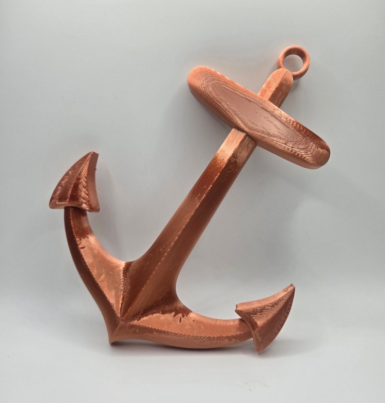 May include: A copper-colored metal anchor with a flat, rectangular top and two pointed arms. The anchor is a decorative item.