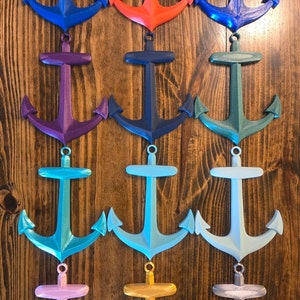 May include: Twelve different colored 3D printed anchor ornaments. The anchors are all the same size and shape, but are painted in different colors, including blue, red, purple, green, teal, light blue, pink, gold, and silver.