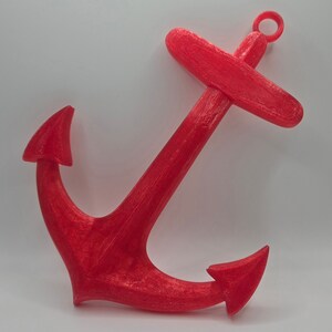 May include: A bright red anchor made of plastic. The anchor has a loop at the top and two points at the bottom.