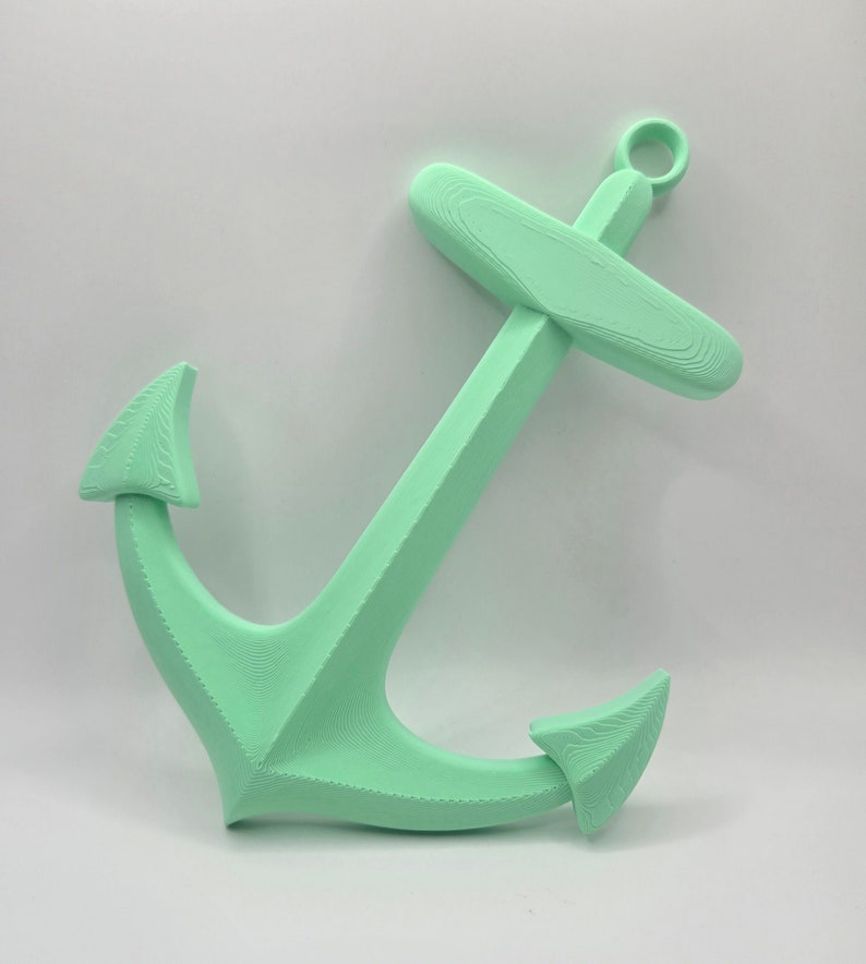 May include: A mint green anchor made of plastic. The anchor has a loop at the top and two points at the bottom.