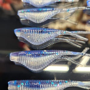 May include: A close-up of five translucent blue and silver glitter fishing lures. The lures are shaped like small fish and have a ribbed texture.