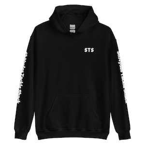 以下が含まれることがあります： 白い文字が入った黒いフード付きスウェットシャツ。「STS」の文字が胸にあり、袖には「St. Andrew's Tackle Shack」の文字が縦にプリントされています。スウェットシャツにはフロントポケットとドローストリングフードが付いています。