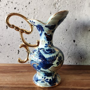 Peut inclure: Un petit pichet en céramique bleu et or avec un motif floral. Le pichet a une poignée délicate et un corps rond.