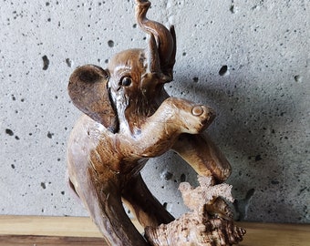 May include: A wooden elephant figurine with a brown and tan finish. The elephant is standing on its hind legs and has its trunk raised. The elephant is holding a seashell in its front legs.