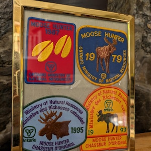 May include: Four framed patches with the text "Moose Hunter" and the years 1987, 1979, 1995, and 1993. The patches are from the Ontario Ministry of Natural Resources.