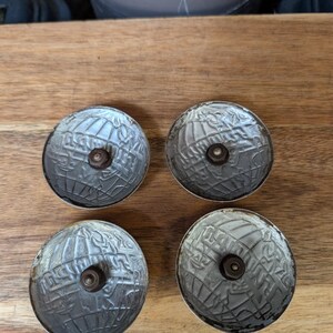 May include: Four antique silver-colored cabinet knobs with a globe design. Each knob has a central screw and a detailed, textured surface. The knobs are arranged on a wooden surface.