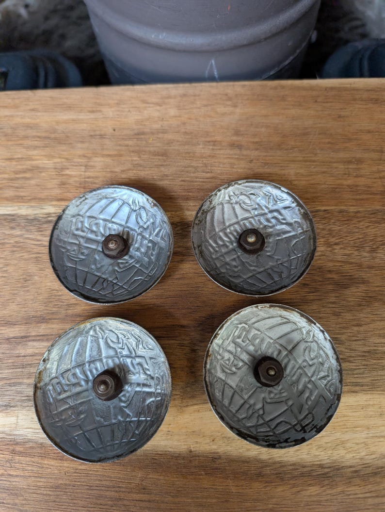 May include: Four antique silver-colored cabinet knobs with a globe design. Each knob has a central screw and a detailed, textured surface. The knobs are arranged on a wooden surface.