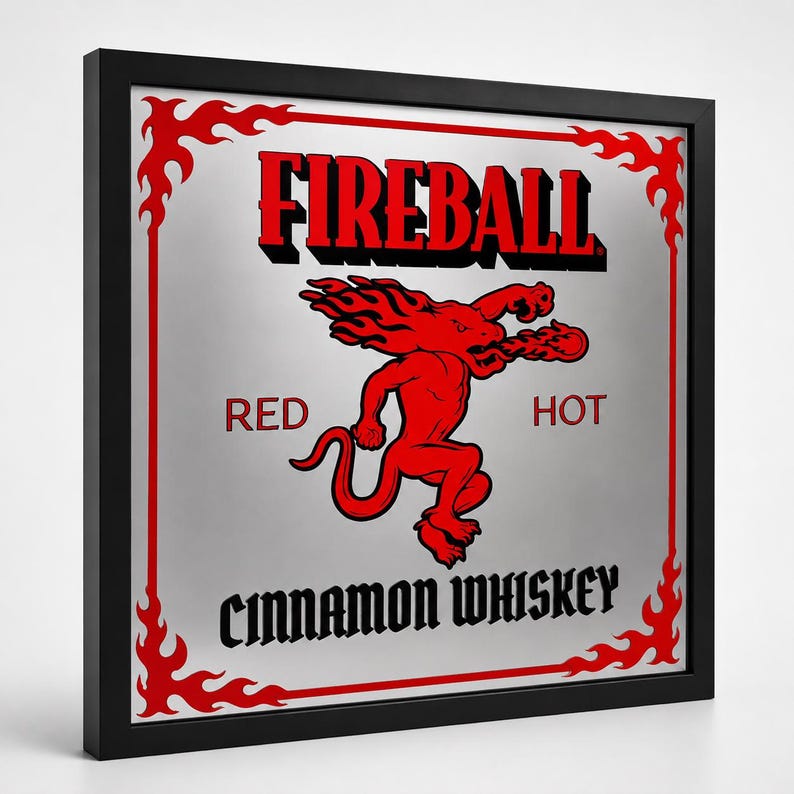 Puede incluir: Un letrero enmarcado con el texto "FIREBALL" en rojo, con un gr&aacute;fico de drag&oacute;n rojo. Las palabras "RED" y "HOT" flanquean al drag&oacute;n, y "CINNAMON WHISKEY" est&aacute; en la parte inferior. El marco es negro.