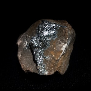 May include: A close-up of a dark brown rock with a silvery-grey mineral deposit. The rock has a rough, uneven surface.