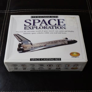 May include: A white box kit labeled "EYEWITNESS KITS SPACE EXPLORATION" with a picture of a space shuttle. The box also says "SPACE CASTING KIT" and includes the text "Discover the awesome world of space travel- cast, paint and display fantastic space vehicles while you read and learn."